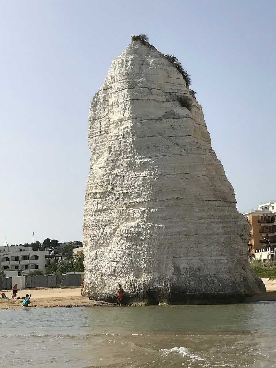Pizzomunno, seen in close-up, viewed from the sea, with bathers at its base, showing scale