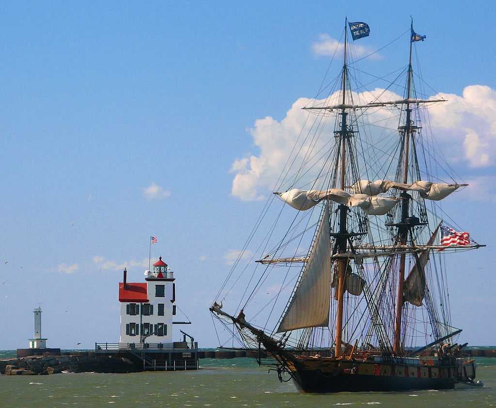 At an Ohio history festival, the 19th-century style brig warship Niagara passes the Lorain lighthouse.